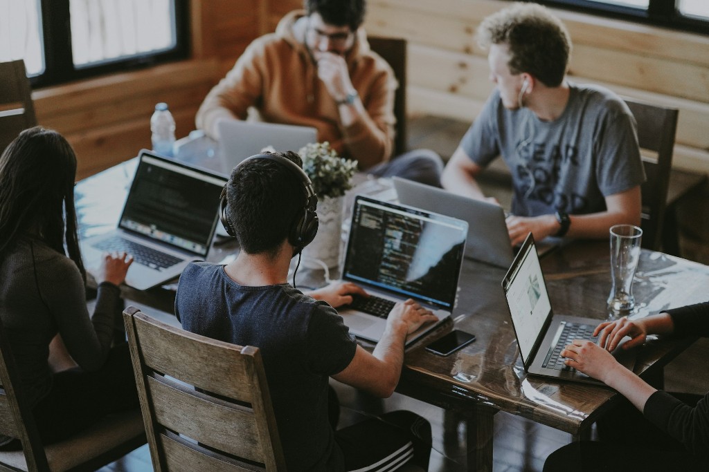 Team collaborating at a shared table with laptops in a bright workspace